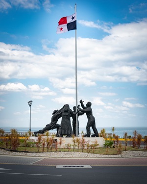 silver Sculpture of people holding a flag against a cloudy blue sky