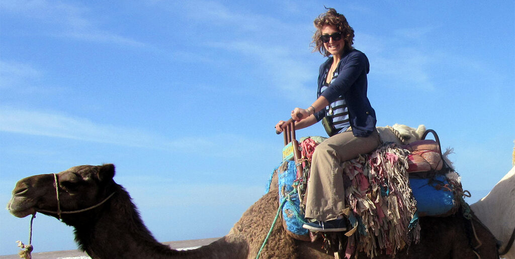 woman in sunglasses in the desert sitting atop a camel